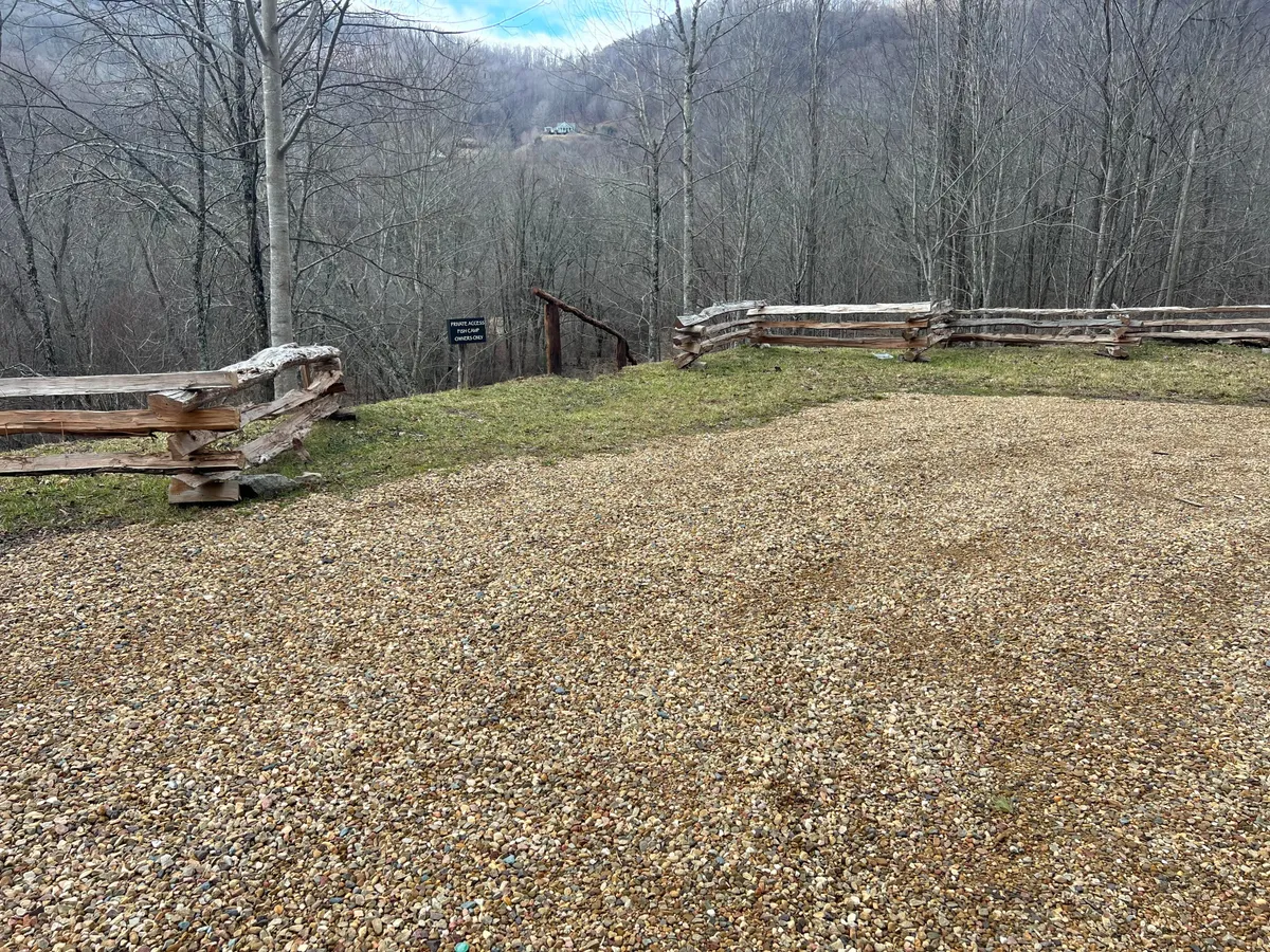 A peaceful gravel area with a wooden fence and bare trees overlooks a stunning mountain view. The open space suggests an ideal spot for picnics, storytelling around a fire pit, or stargazing under the wide sky.