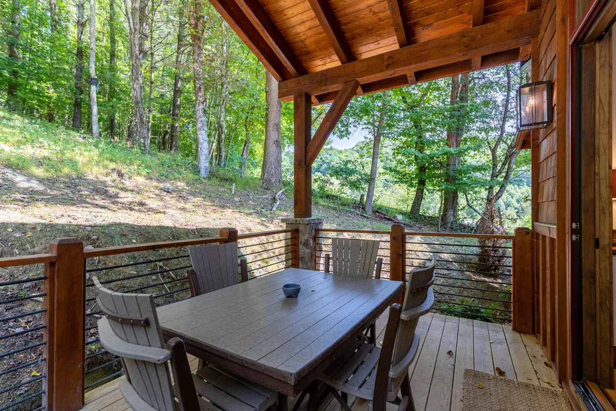A wooden deck sits nestled among trees, with a large dining table and panoramic mountain vistas. The scene is set for outdoor dining or relaxing in the fresh mountain air, inviting guests to extend their living space beyond the indoors.