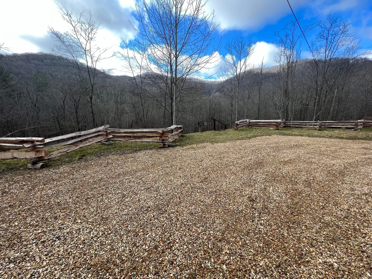 This image features an inviting outdoor area with a gravel space, wooden fence, surrounding trees, and impressive mountain views. The scene evokes a gathering space ideal for stargazing or sharing stories around a fire pit, even though the fire pit itself is not directly visible.