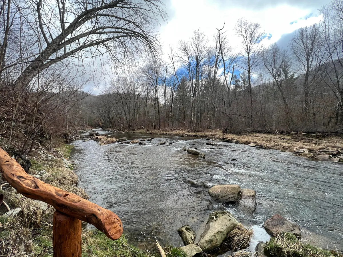 A tranquil view of the flowing river framed by a sturdy wooden railing, backed by lush landscapes. The serene setting is ideal for fishing, hiking, and picnicking, and underscores the natural beauty and exclusive river access available at Eagles Nest.