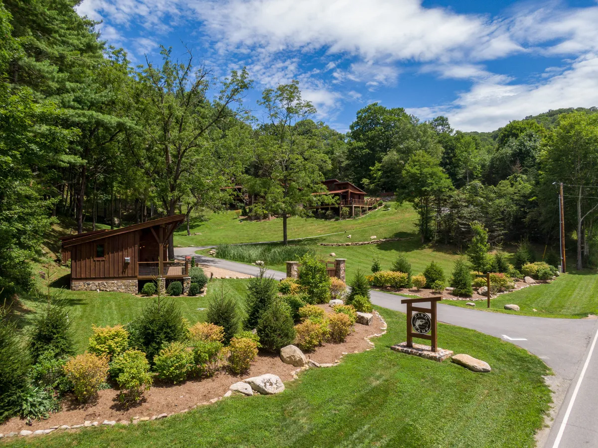 A wooden cabin is surrounded by landscaped gardens and open grassy spaces, with a road leading through the property. The atmosphere is tranquil and perfect for family gatherings or relaxed evenings outdoors.
